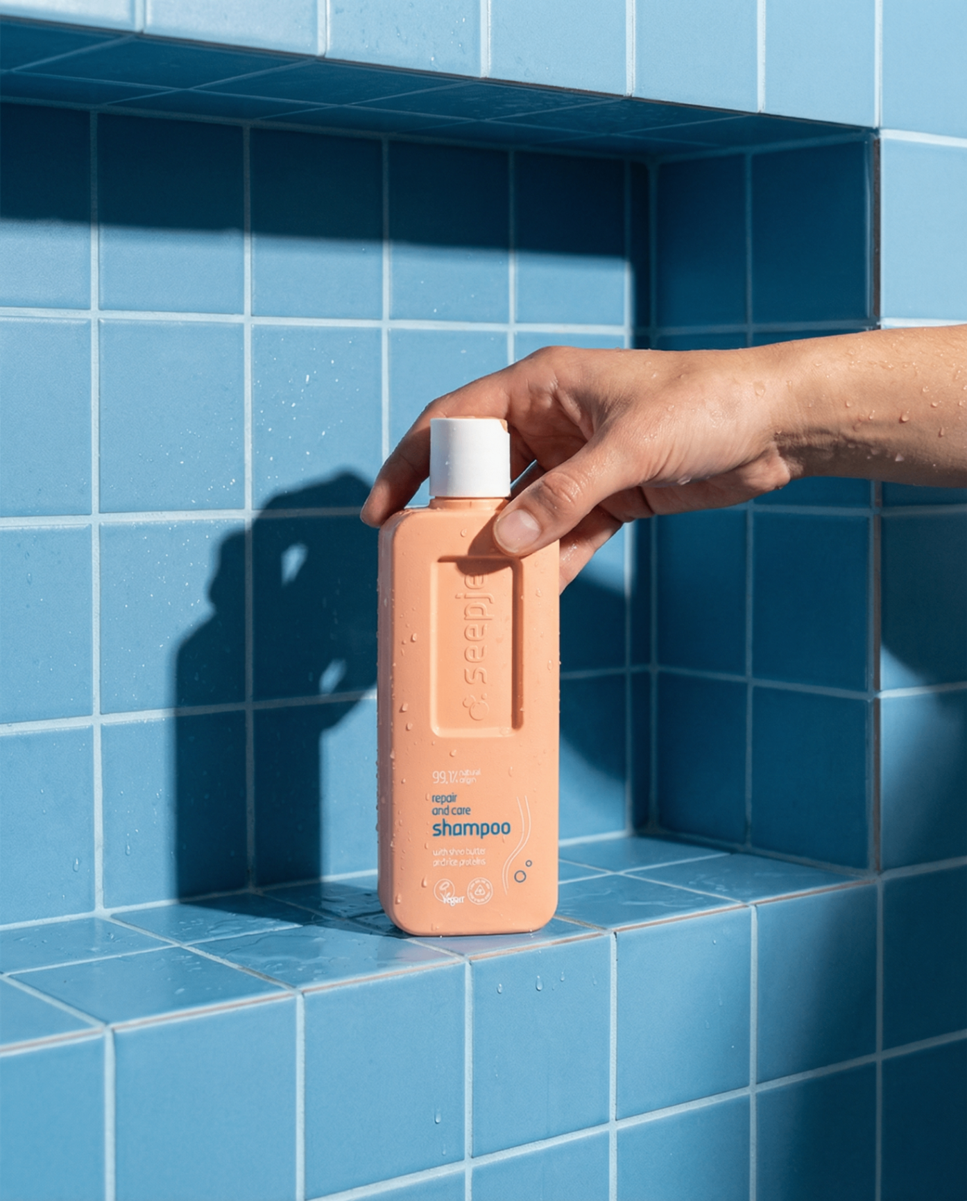 Hand grabbing Seepje shampoo in blue tile corner